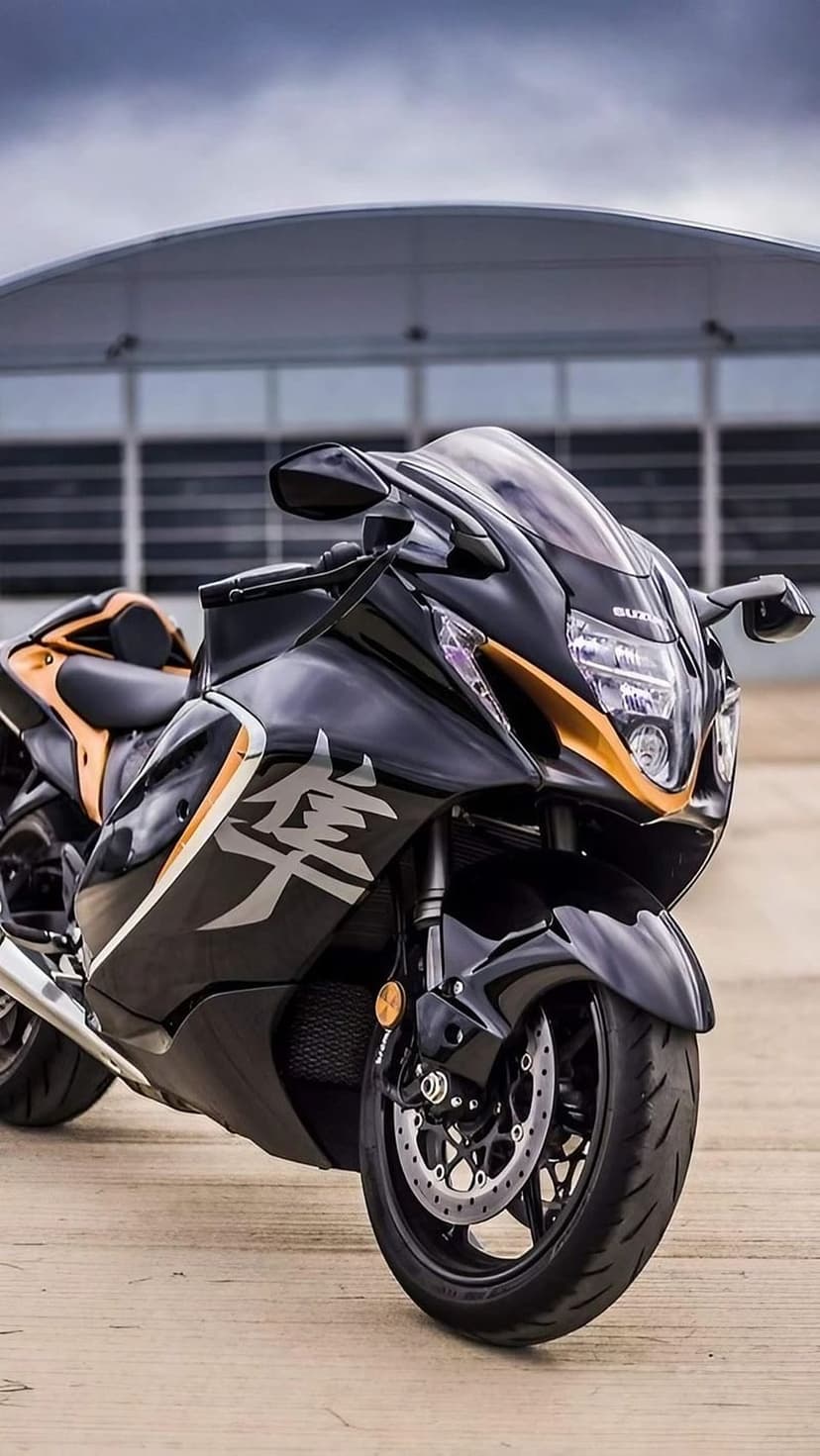 Black Suzuki Hayabusa motorcycle with gold accents parked on a wooden surface before a modern curved building.