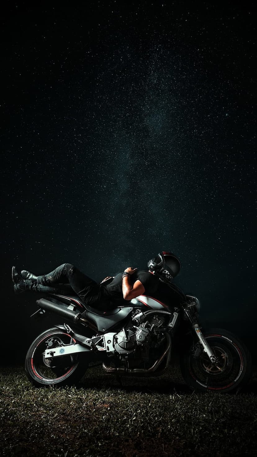 Biker in full riding gear reclines on a motorcycle seat beneath a dense field of shimmering night stars.