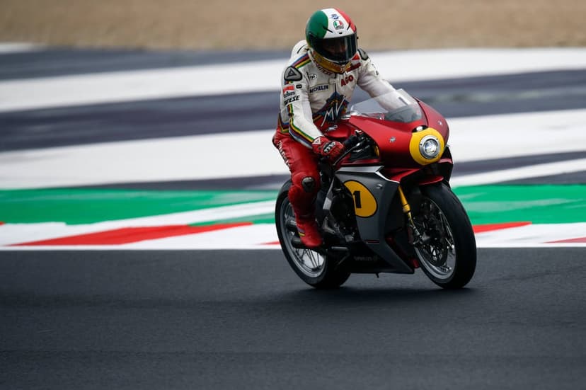 A racer on a red and silver MV Agusta motorcycle maneuvers through a turn on a colorful racetrack.