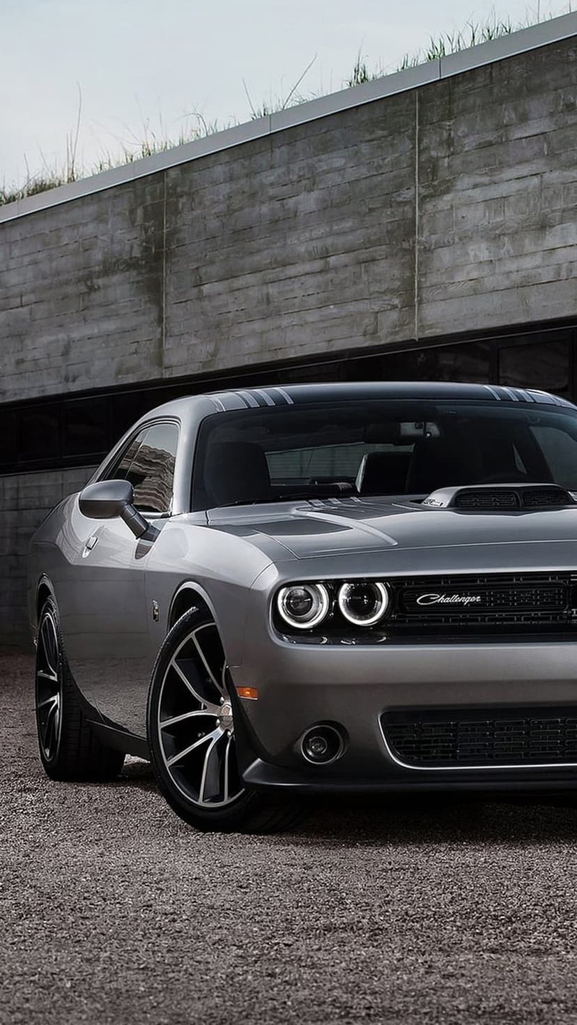 Silver Dodge Challenger with halo ring headlights and racing stripes parked in front of a concrete building.