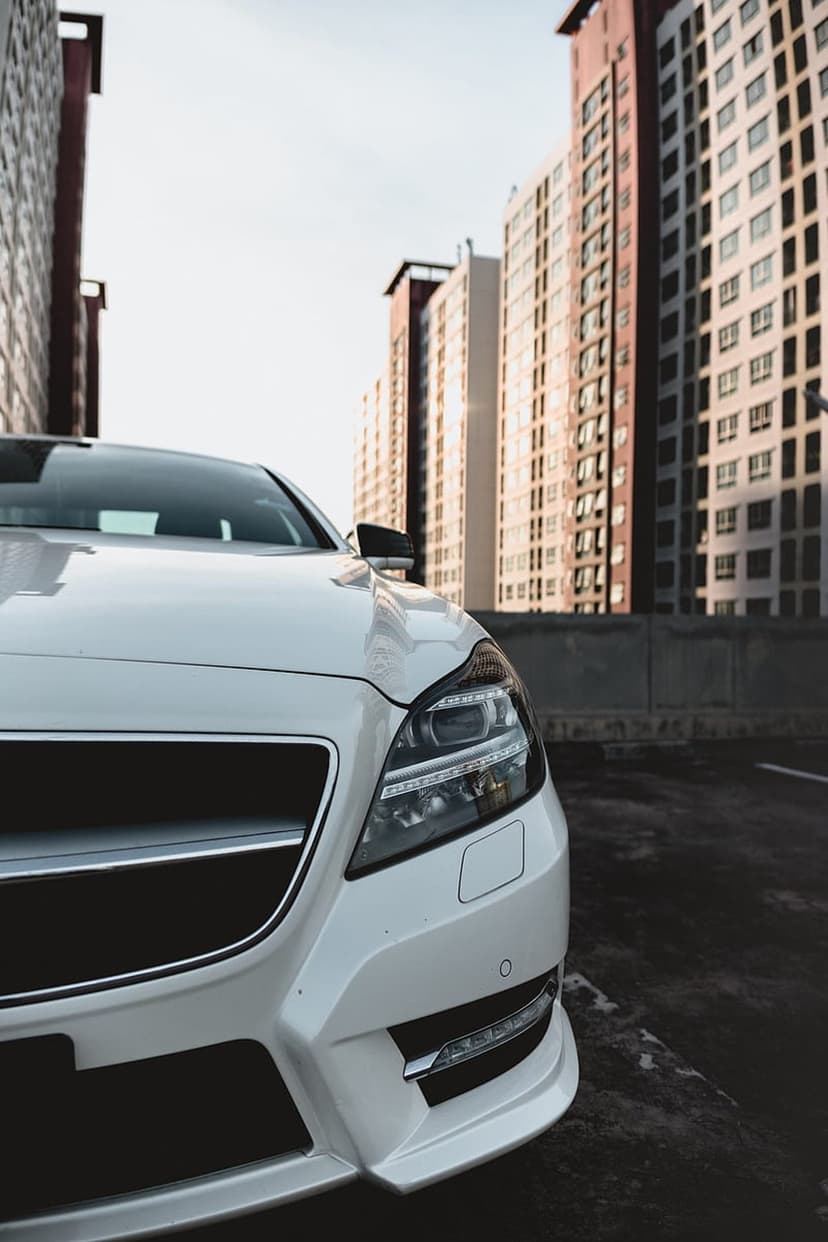 White Mercedes-Benz CLS luxury sedan parked in front of modern brown and tan apartment buildings in soft daylight.