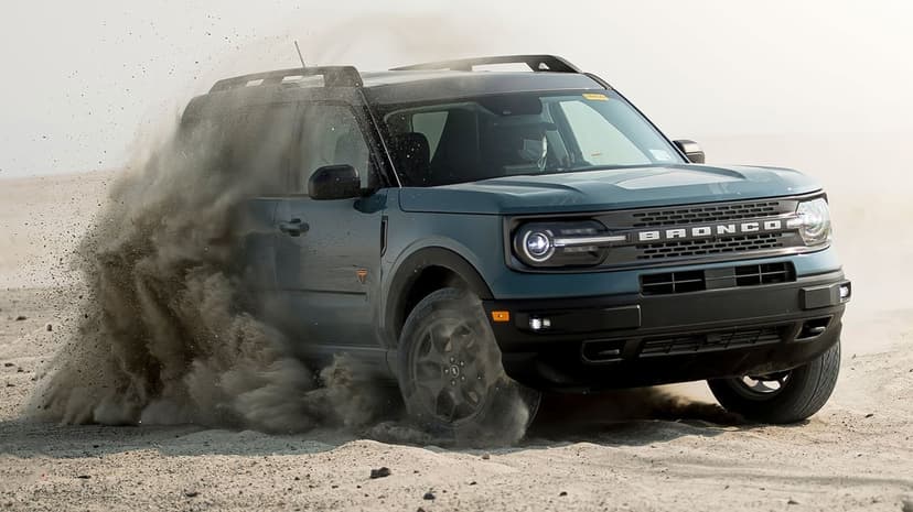 Ford Bronco Sport kicking up a massive sand cloud while off-roading in a bright desert landscape.
