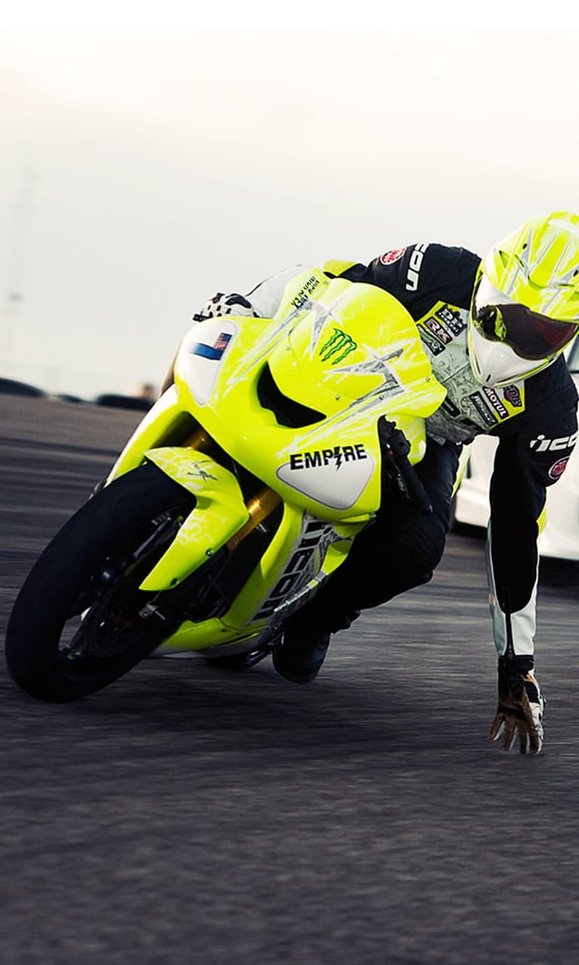 Motorcyclist in yellow racing gear leans a neon sportbike into a sharp asphalt turn with visible motion blur.