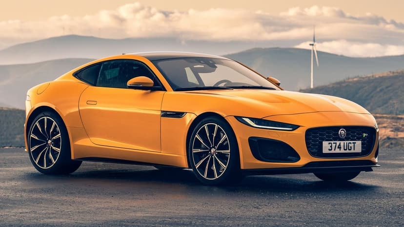 Yellow Jaguar F-Type sports coupe parked on a mountain road with a wind turbine and cloudy sky in the background.