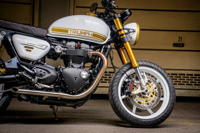 Custom white Triumph Speed Twin 1200 motorcycle with gold forks and stripes in a minimalist garage setting.