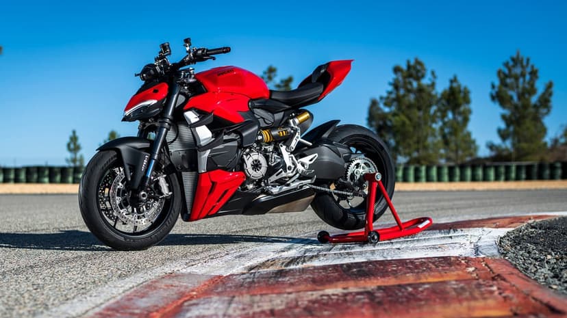 Red Ducati motorcycle on a rear stand on a sunny racetrack under a clear blue sky with painted curbs.