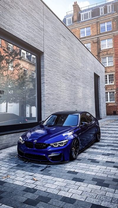Blue BMW M4 parked on cobblestone street in front of modern building