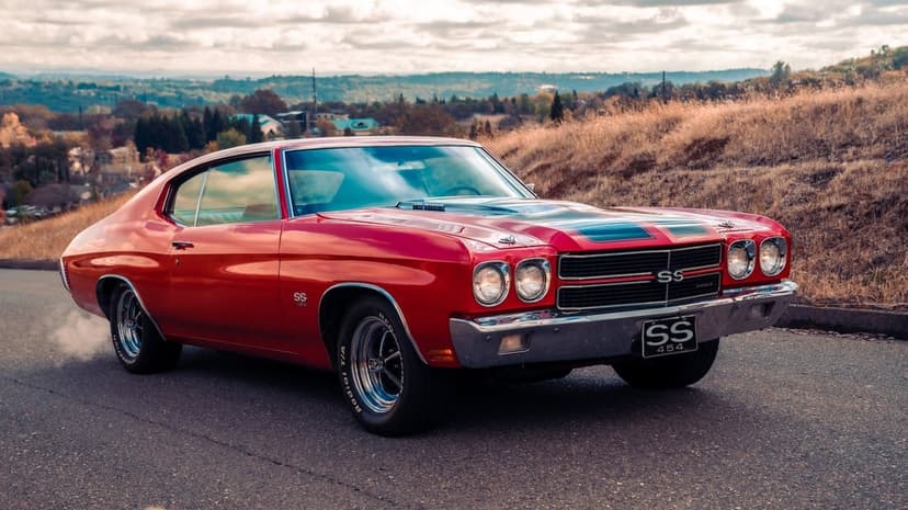 Red 1970 Chevrolet Chevelle SS 454 muscle car with black stripes parked on an asphalt road near a dry grassy hill.