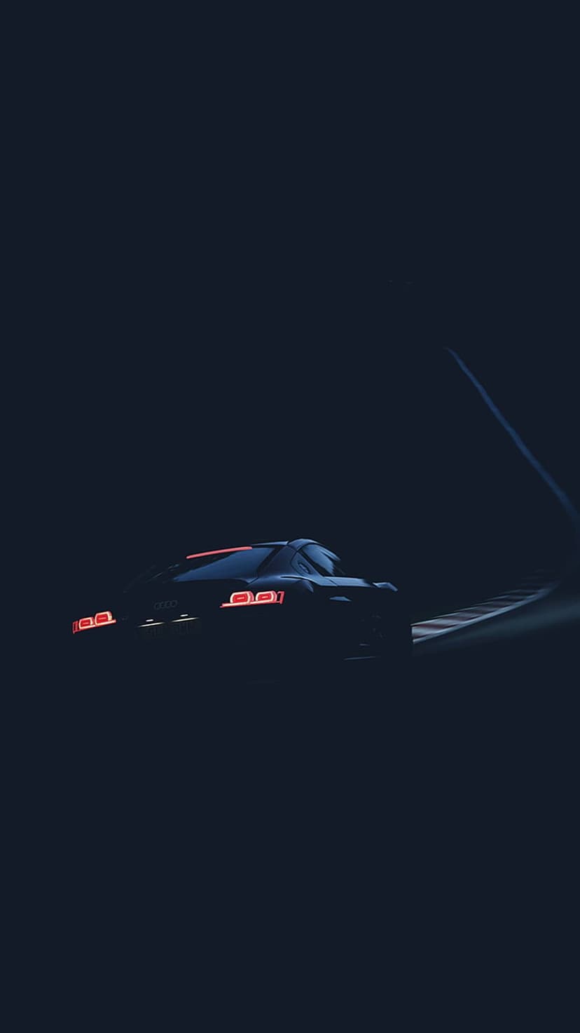 Audi R8 supercar with glowing red tail lights speeds along a dark race track under midnight blue lighting.