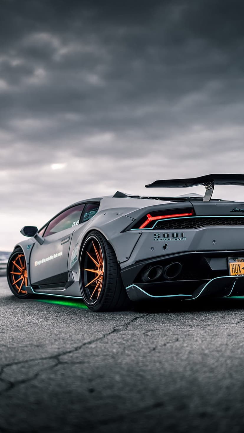 Lamborghini Huracan featuring a widebody kit, orange wheels, and green underglow against a moody cloudy sky.