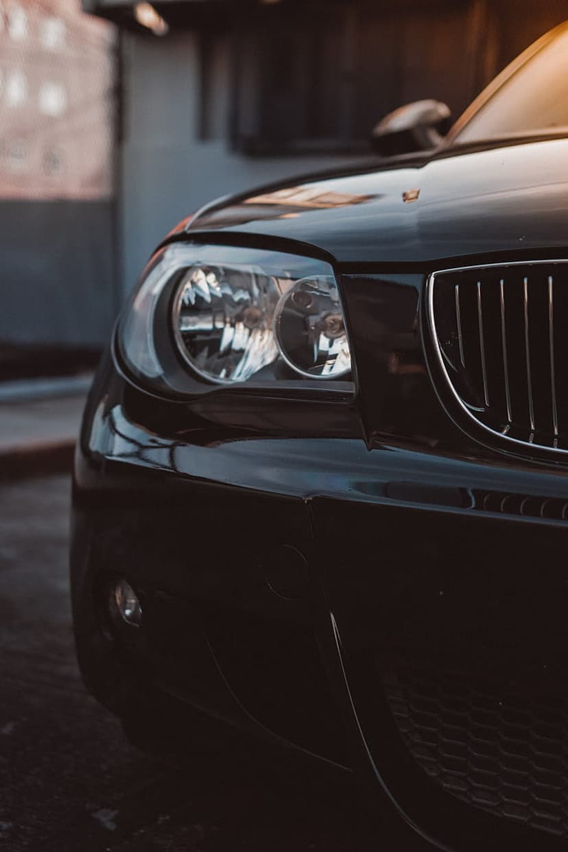 Black luxury car headlight and vertical grille shown in a low-angle close-up with dramatic lighting and reflections.
