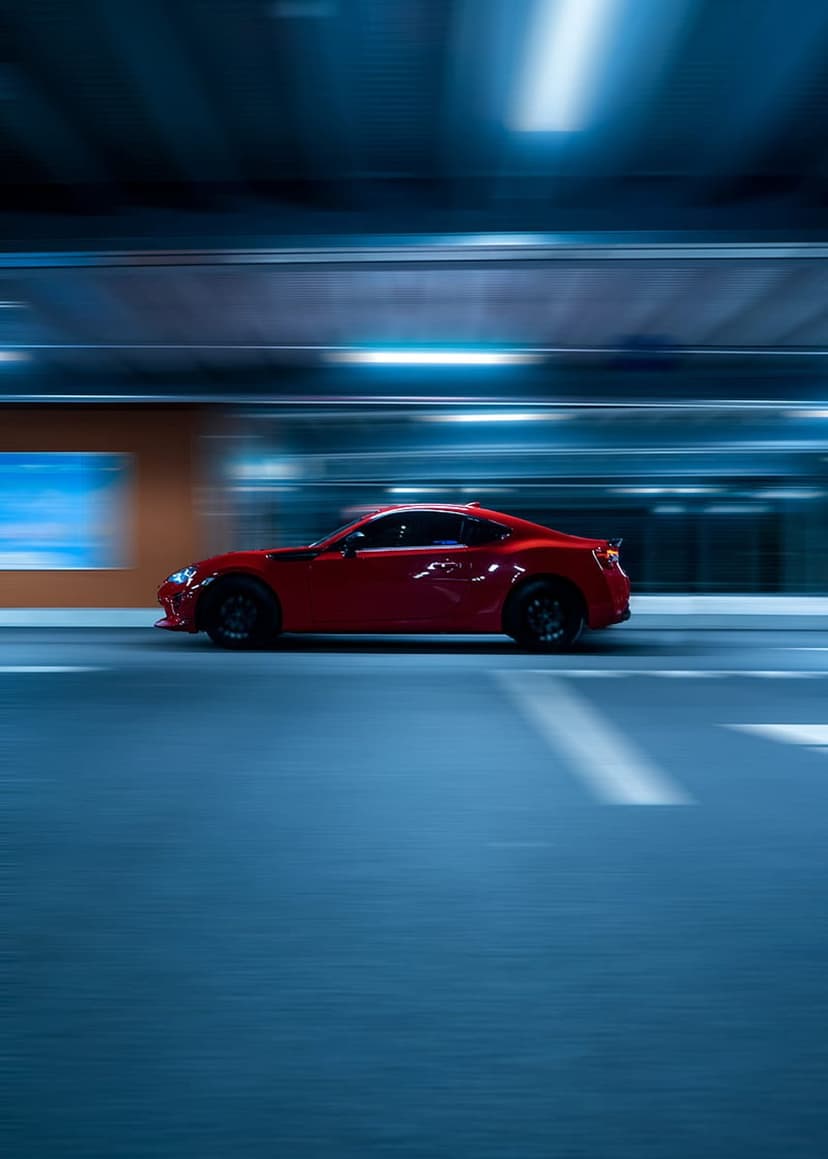 Red sports car racing through a glowing blue tunnel with heavy motion blur and reflective metallic surfaces.