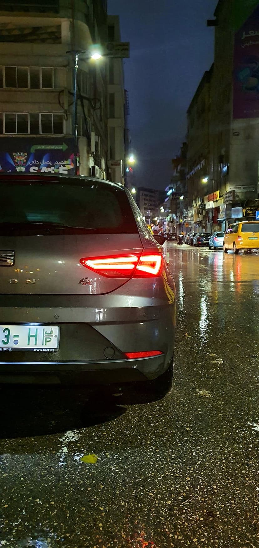 Red taillights of a car glow on a wet city street at night with reflections on the rain-soaked asphalt.