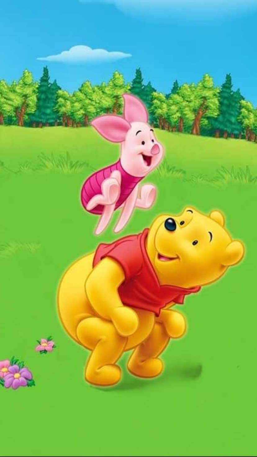 Winnie the Pooh and Piglet leap over blooming wildflowers in a sunny forest clearing under a bright blue sky.