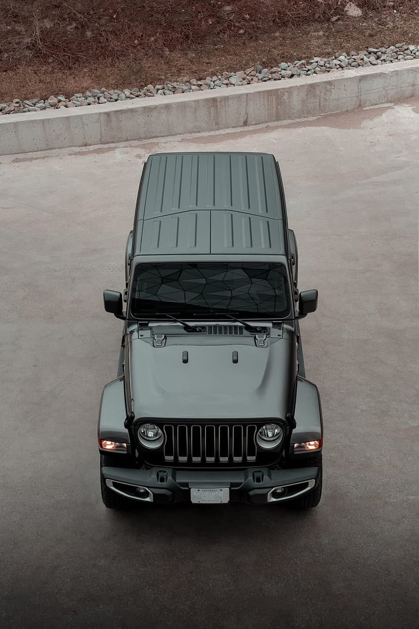Dark gray Jeep Wrangler seen from above on a concrete surface with its ribbed hardtop and round headlights visible.