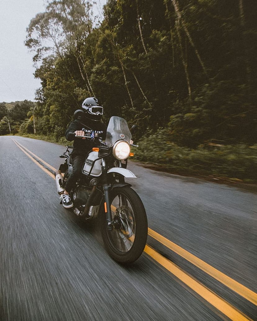Motorcyclist in white riding gear leans an adventure bike on a curved road through a dense green forest.