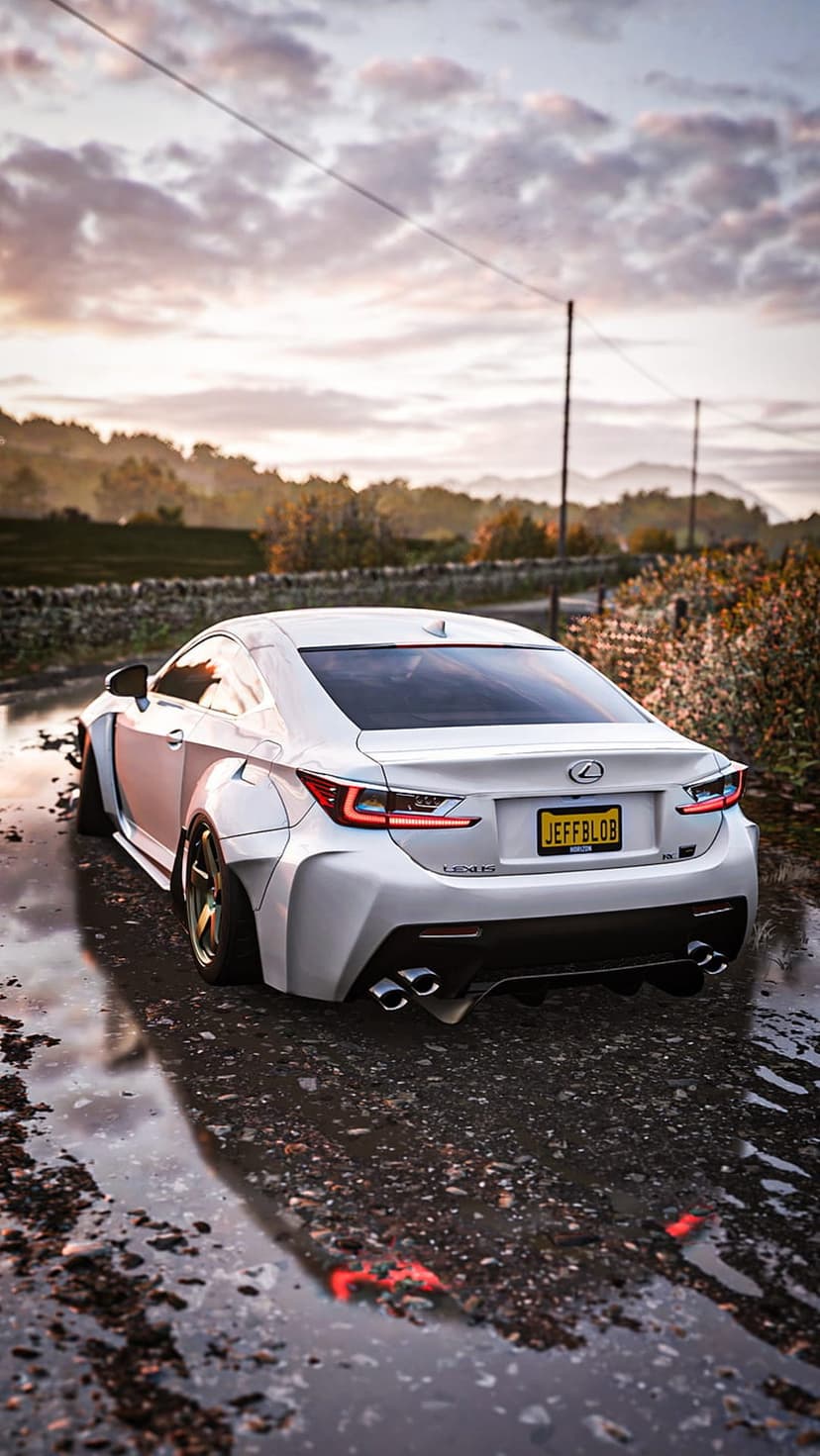 White Lexus RC F with widebody fenders parked on a wet asphalt road under a dramatic orange and purple sunset sky.
