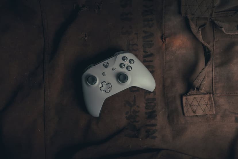 White Xbox controller on a dark, worn fabric surface with moody lighting highlighting the joysticks and buttons.