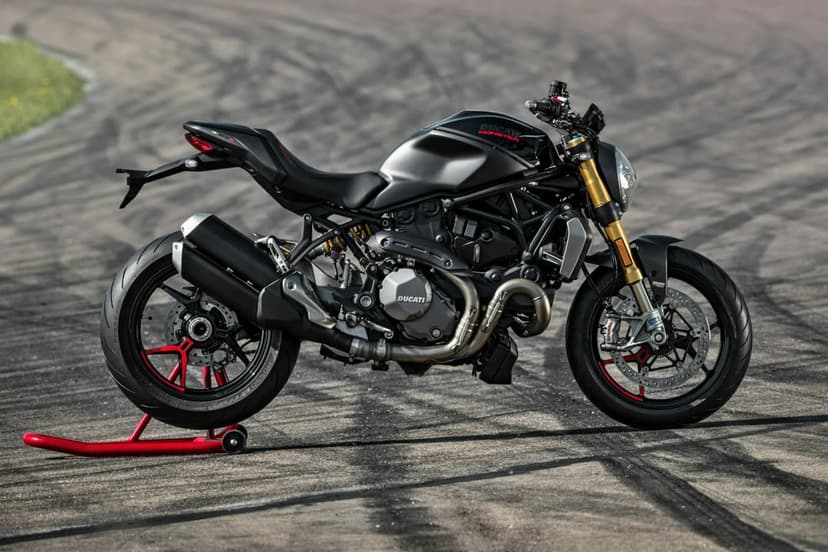 Matte black Ducati Monster motorcycle on a red rear stand parked on an asphalt track with golden front forks.
