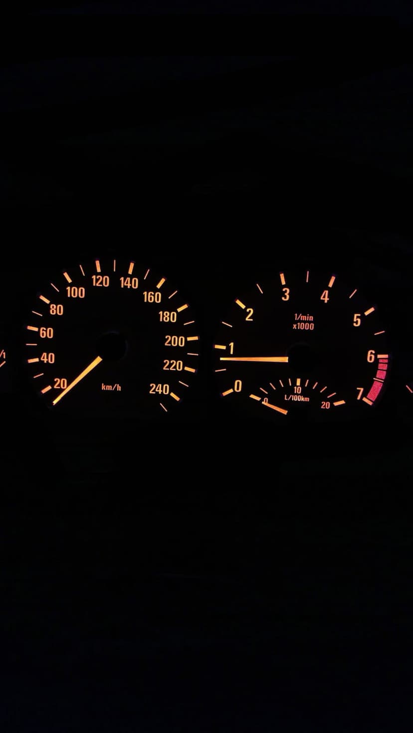Glowing orange speedometer and tachometer dials shine against a dark vehicle interior during a night drive.