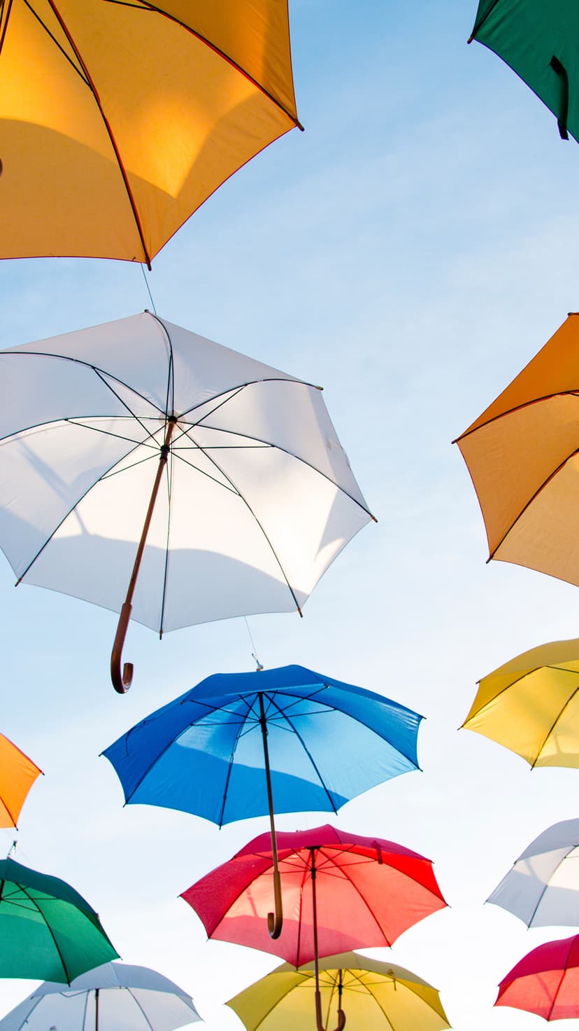 Multicolored umbrellas including red, blue, and orange float against a clear sky in a vertical perspective.