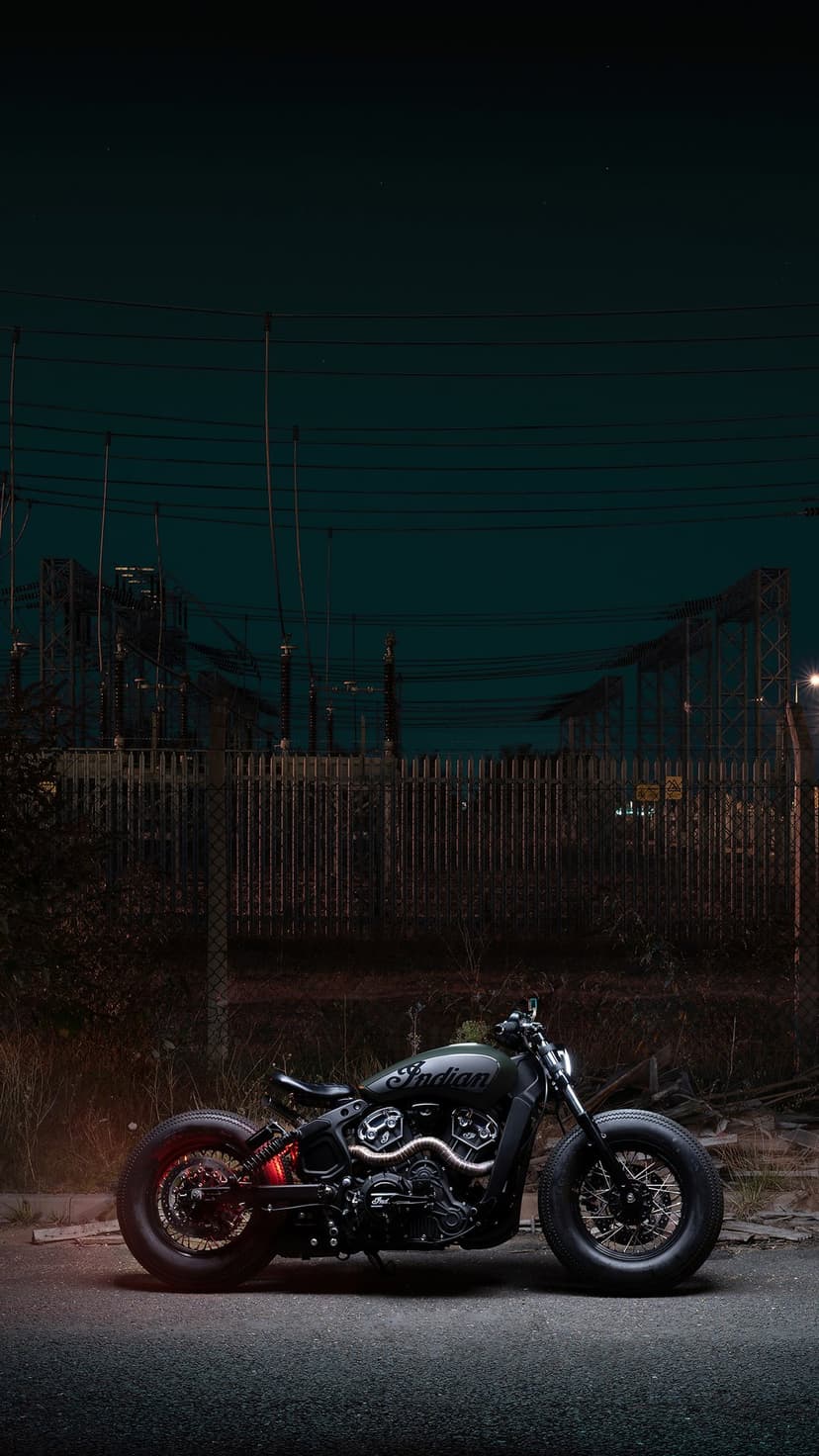 Custom black Indian motorcycle parked in an industrial zone under power lines during a hazy twilight dusk.