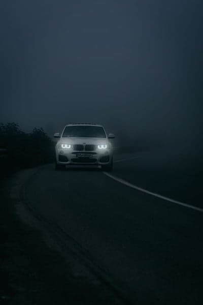 White BMW SUV Navigating Foggy Night Road Mobile Wallpaper