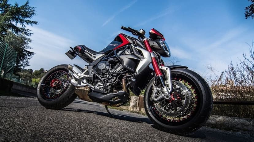 Red and silver MV Agusta motorcycle with spoke wheels on an asphalt road against a clear blue sky background.