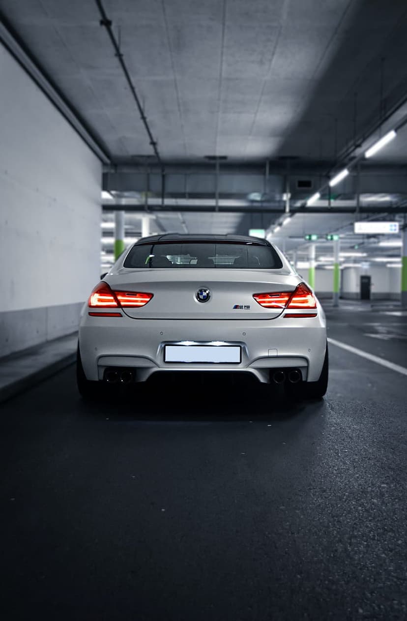 White BMW M6 rear exterior with glowing red taillights in a dark, concrete parking structure under dim lights.