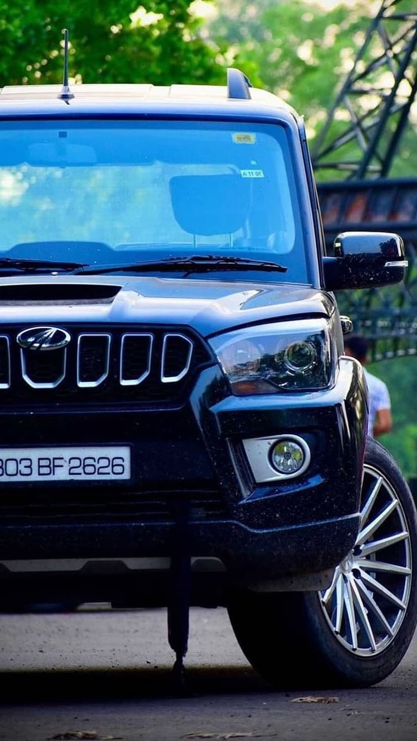 Black Mahindra Scorpio SUV front view with custom alloy wheels, chrome grille, and headlights in an outdoor setting.