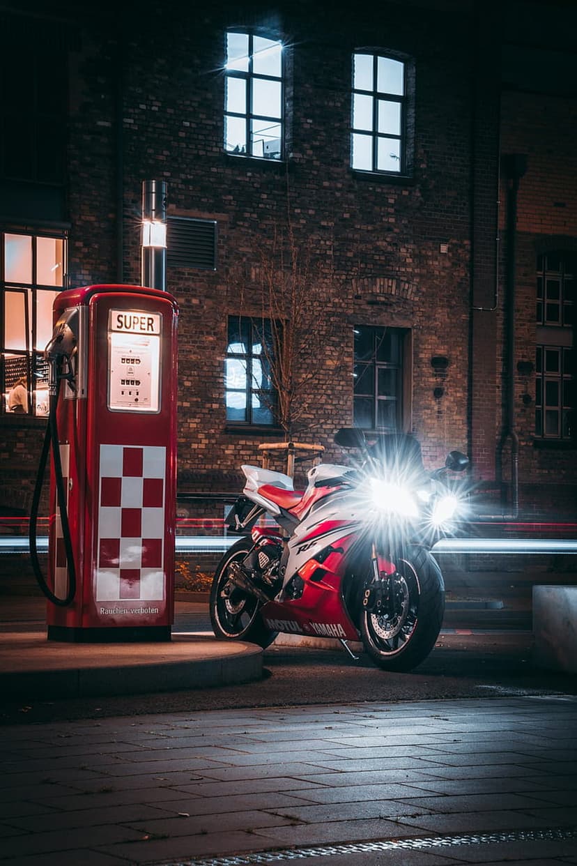 Red Yamaha sportbike parked next to a retro checkered gas pump with glowing headlights under night street lamps.