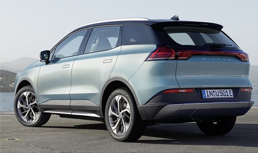 Rear view of a light blue electric SUV with a black roof parked on asphalt near a calm sea under a clear sky.