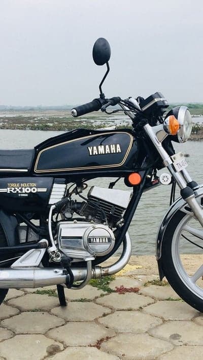 Classic Yamaha RX100 motorcycle by a tranquil water body