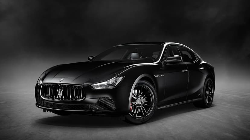 Black Maserati Ghibli luxury sedan with chrome grille and dark wheels in a smoky studio with dramatic lighting.