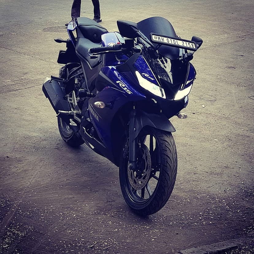 Yamaha R15 V3 blue sportbike parked on a grey paved road with sharp LED headlights and aerodynamic fairings visible.