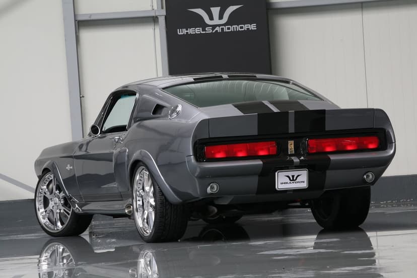 Rear view of a gray classic Shelby GT500 muscle car with black racing stripes and polished chrome rims in a studio.