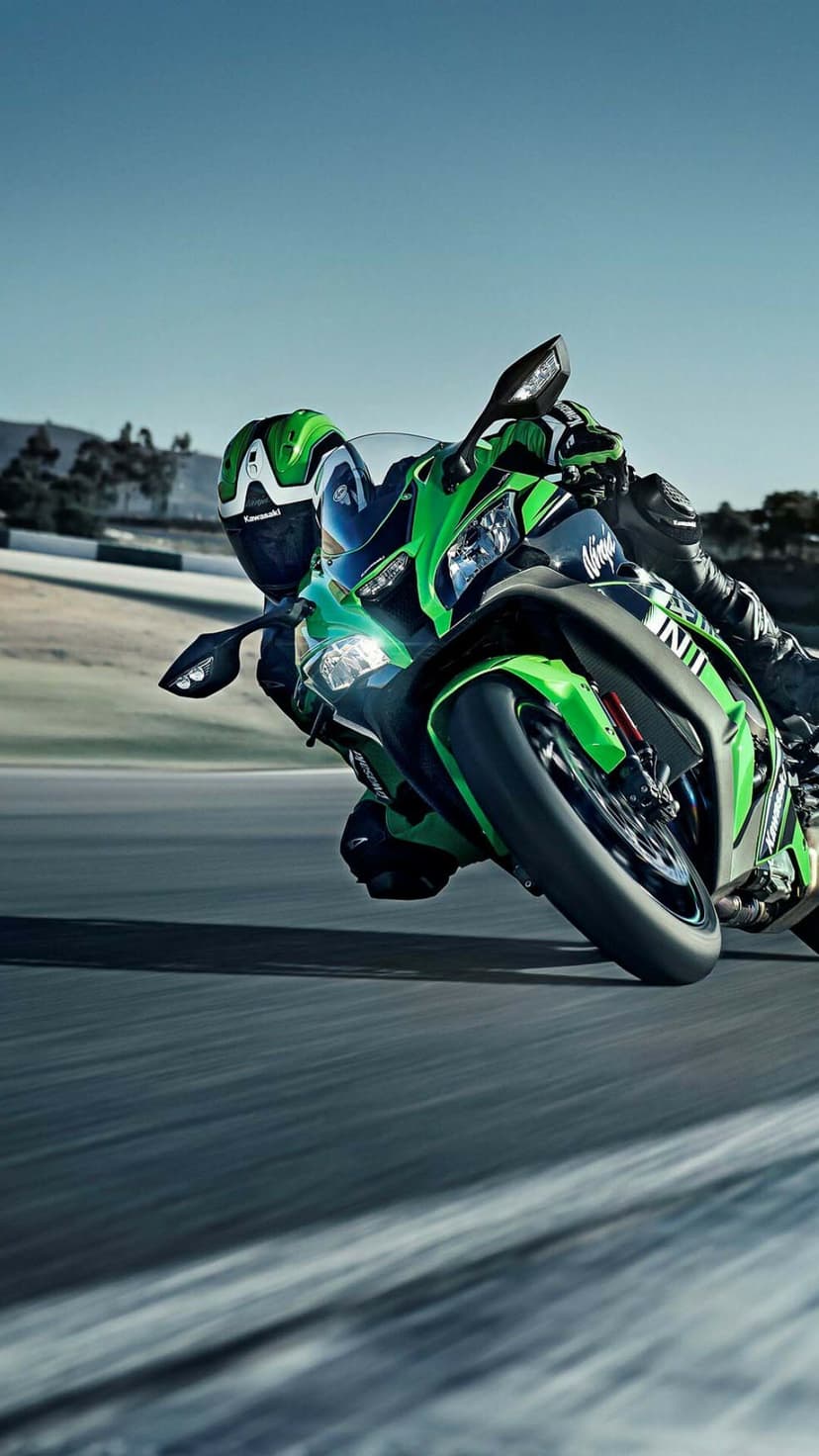 Green Kawasaki Ninja sportbike leaning deep into a racetrack turn with a rider in full racing gear.