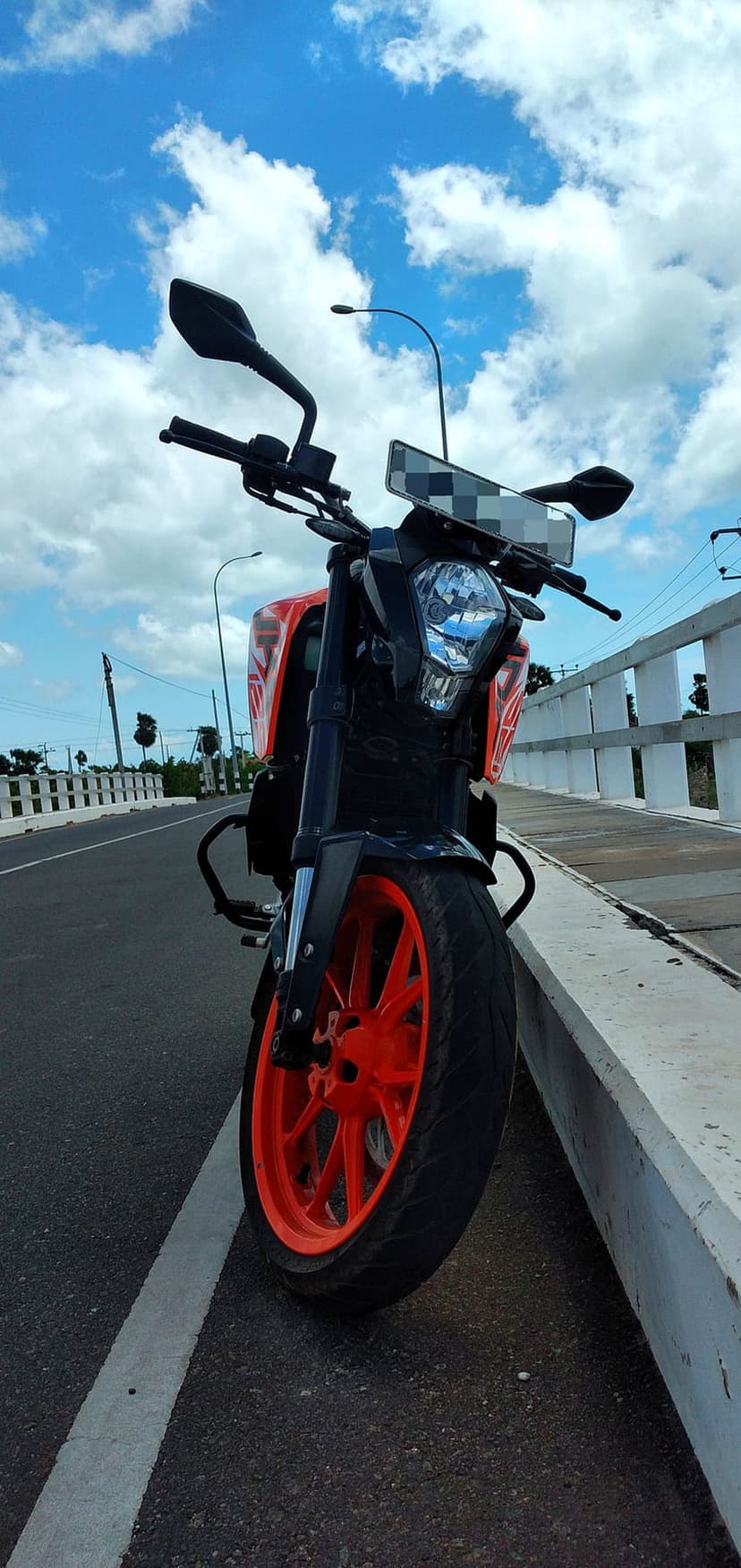 Orange KTM Duke motorcycle with vibrant wheels parked on a highway road against a blue sky with white clouds.