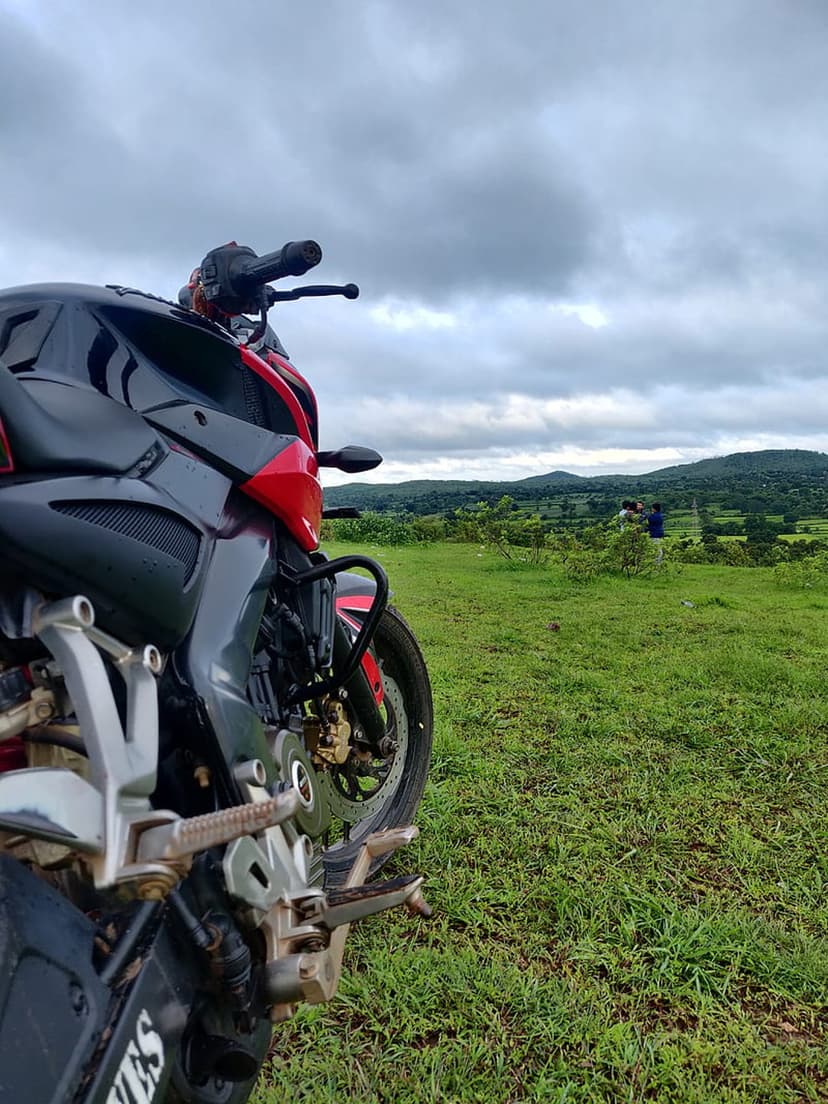 Red and black motorcycle parked on a lush green hill under a dramatic overcast sky with distant rolling hills.