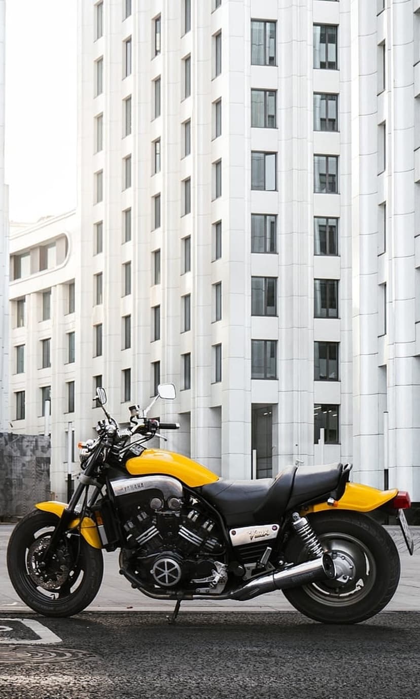 Yellow Yamaha VMAX motorcycle parked on an asphalt street in front of a white contemporary building with windows.