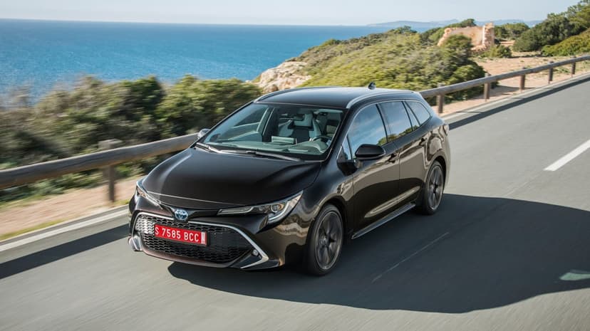 Black Toyota Corolla Touring Sports wagon driving on a coastal road overlooking the bright blue sea.