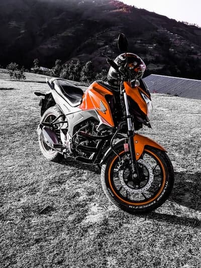 Orange motorcycle parked on grassy hill with mountain background