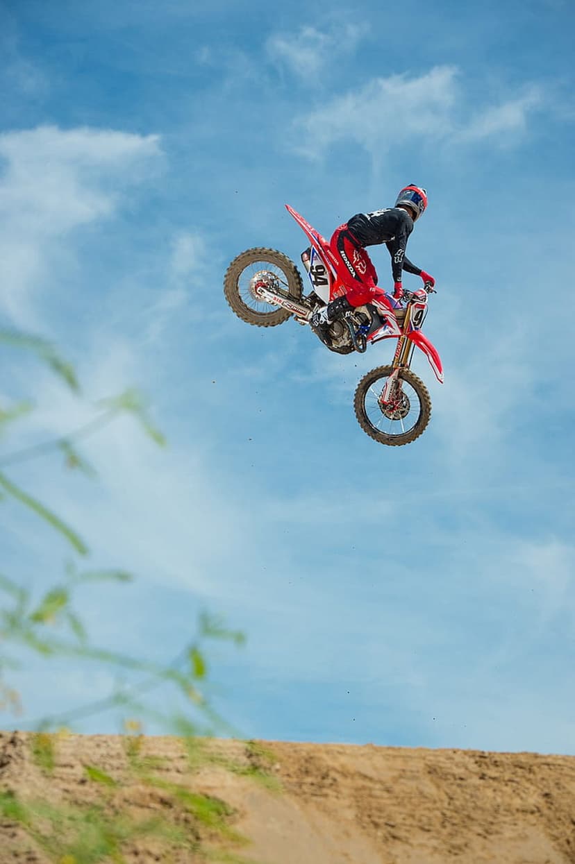 Motocross rider on a red motorcycle suspended mid-air against a bright blue sky during an extreme stunt jump.