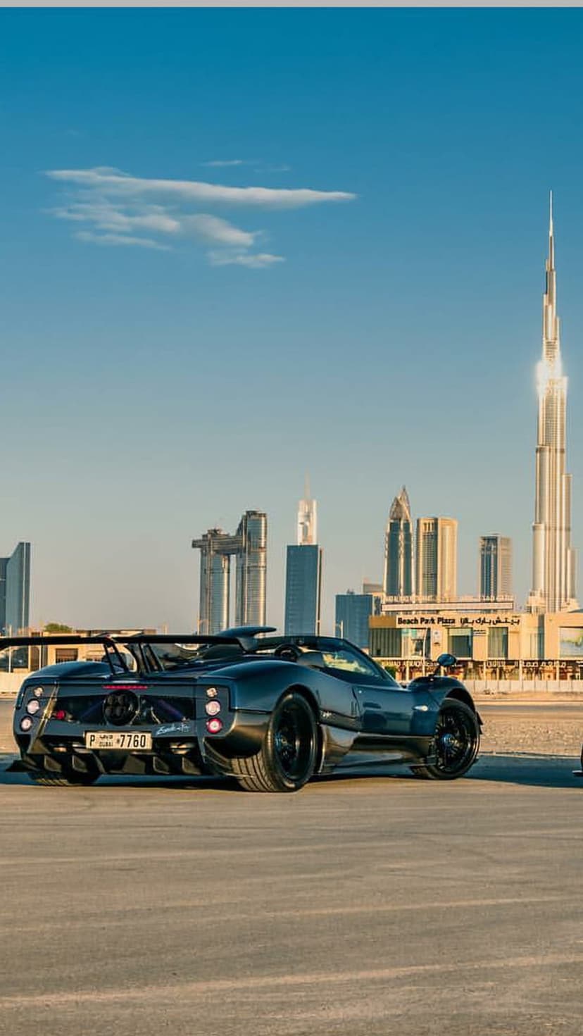 Dark Pagani hypercar parked on asphalt with the Burj Khalifa and Dubai city skyline under a clear blue sky.