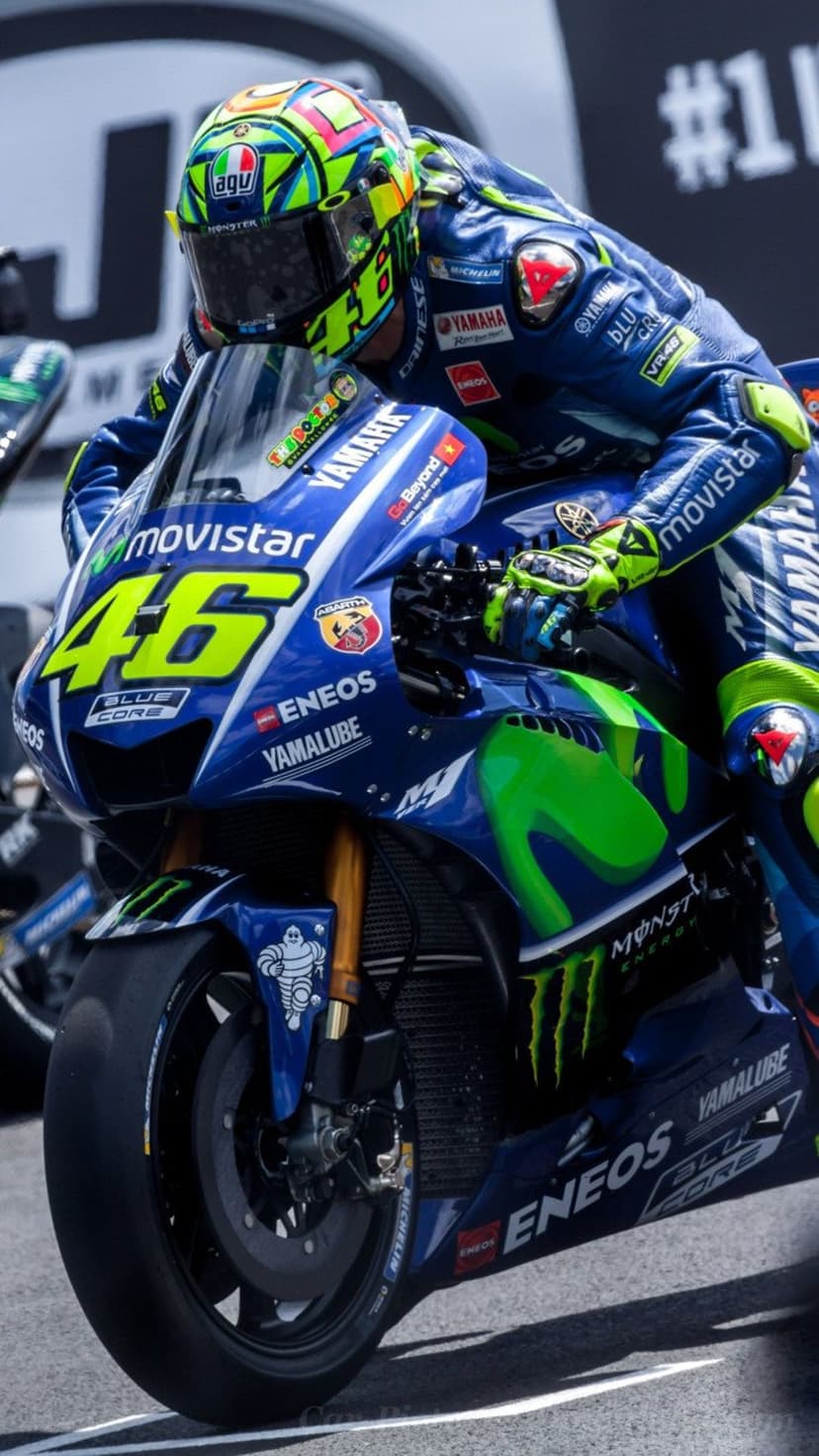 Valentino Rossi in a yellow helmet leans a blue Yamaha motorcycle into a turn during a professional race.