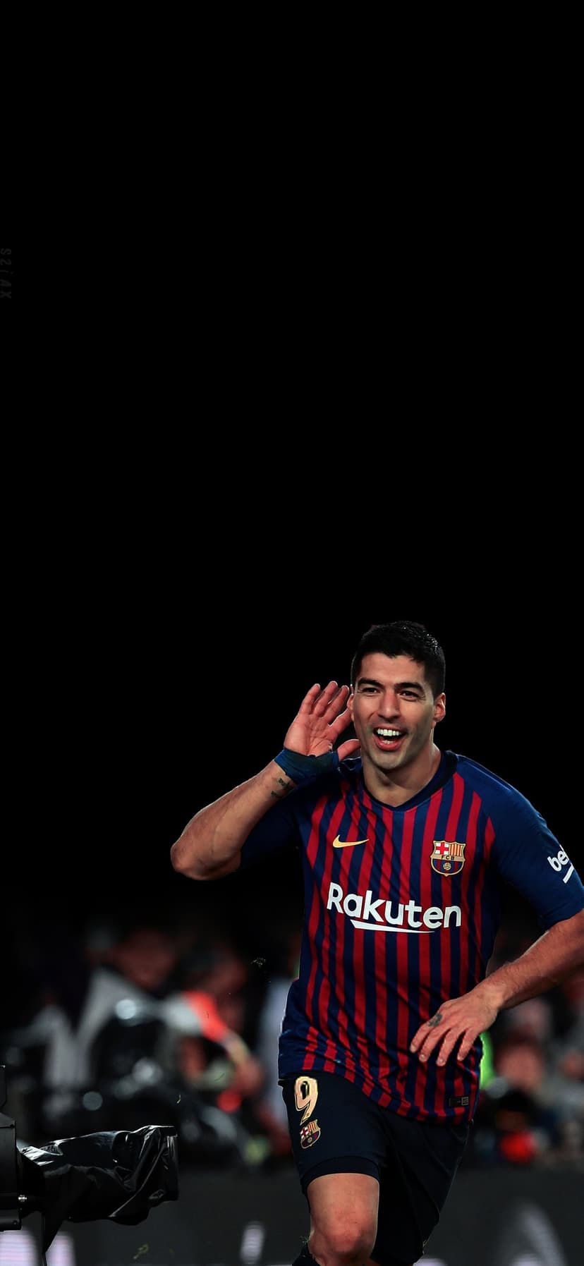 Luis Suarez in a Barcelona jersey raises a hand to his ear while celebrating a goal in a packed football stadium.