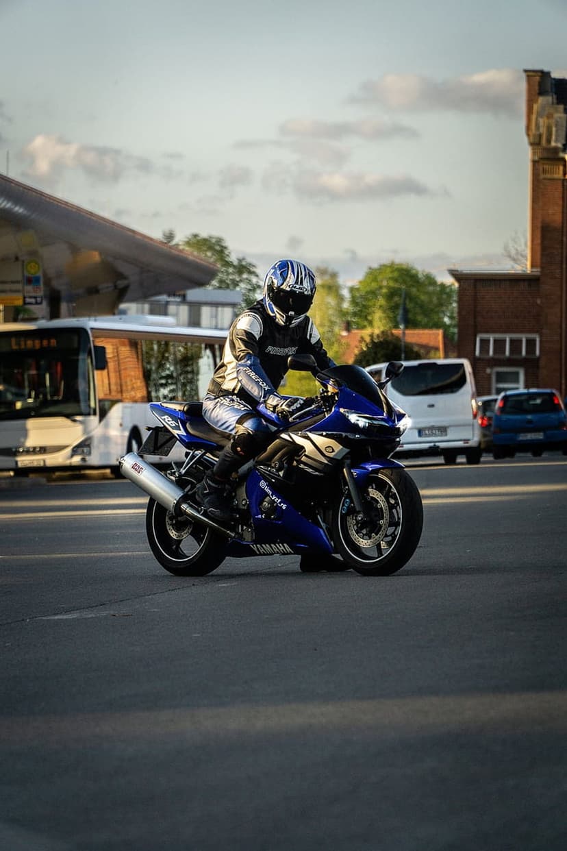 Motorcyclist in blue racing gear leans on a Yamaha sportbike while riding through a busy urban street at daytime.