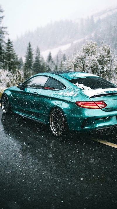 Vibrant Teal Coupe on Snowy Alpine Road Phone Background