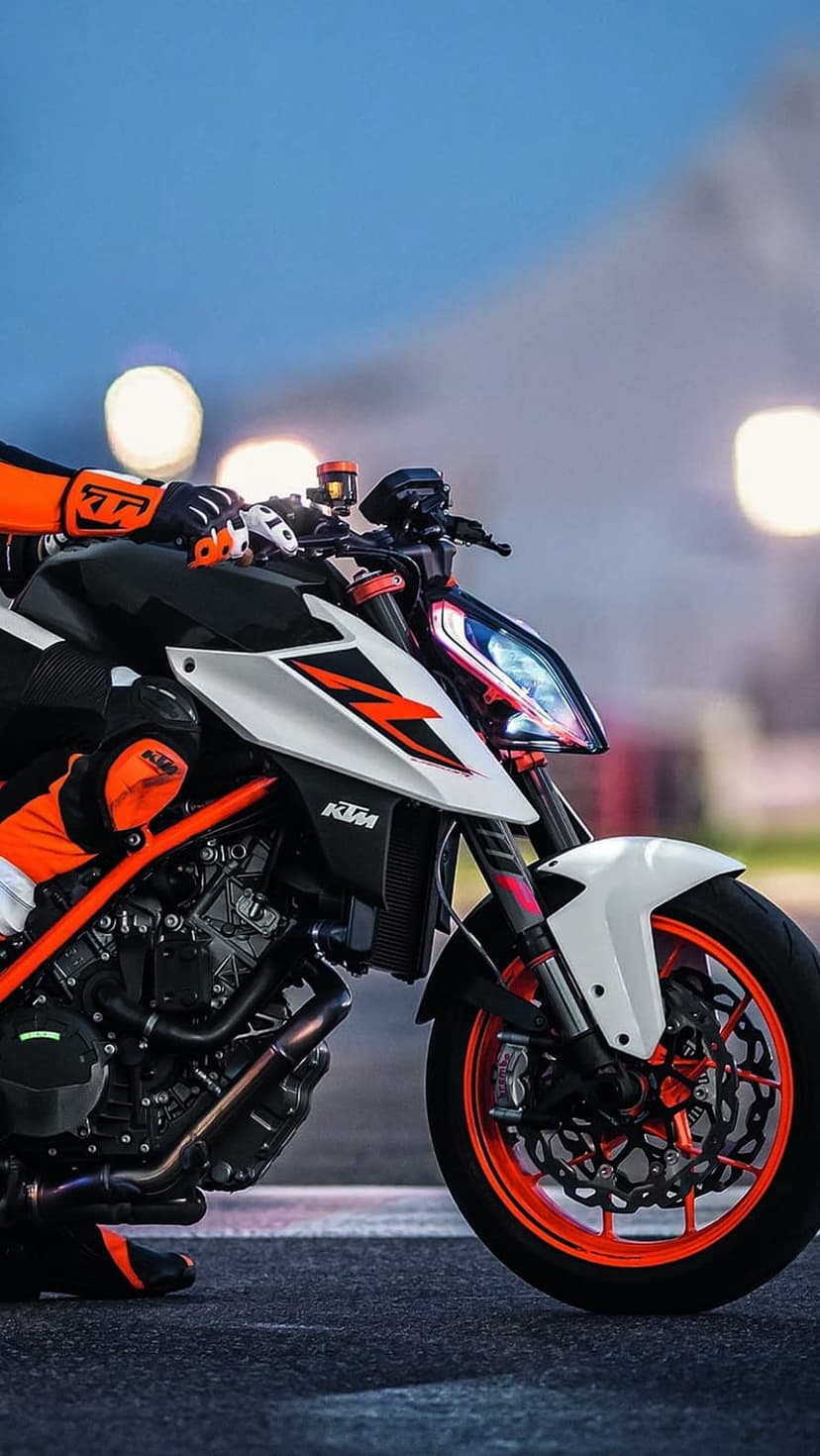 KTM motorcycle rider in orange racing gear leans on a street bike with glowing LEDs against city bokeh.