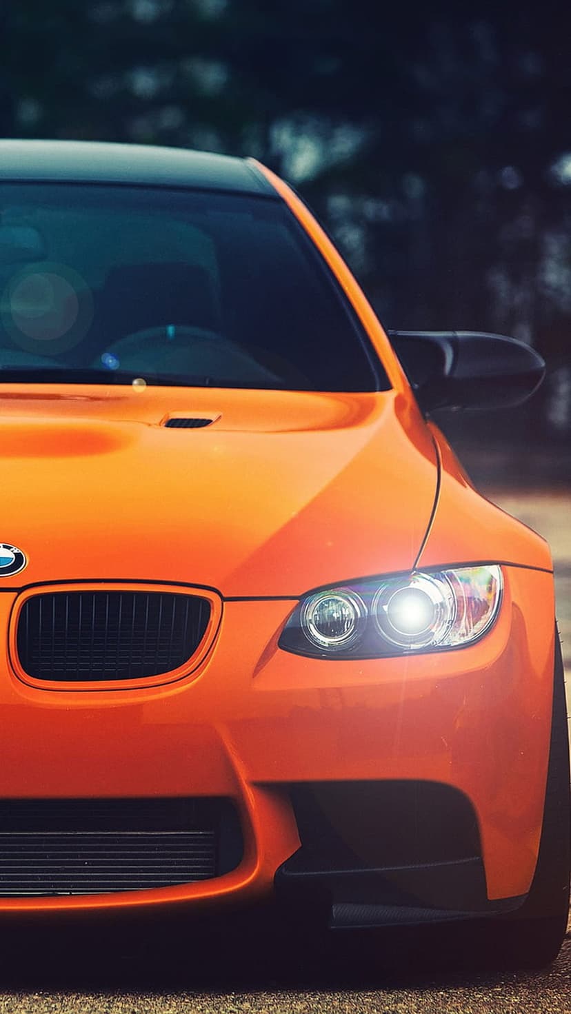 Orange BMW M3 front end featuring glowing LED headlights, black kidney grille, and sharp hood aerodynamic lines.